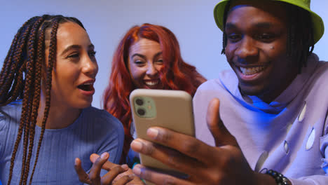 Close-Up-Studio-Shot-Of-Young-Gen-Z-Friends-Sitting-On-Sofa-Sharing-Social-Media-Post-On-Mobile-Phones-2
